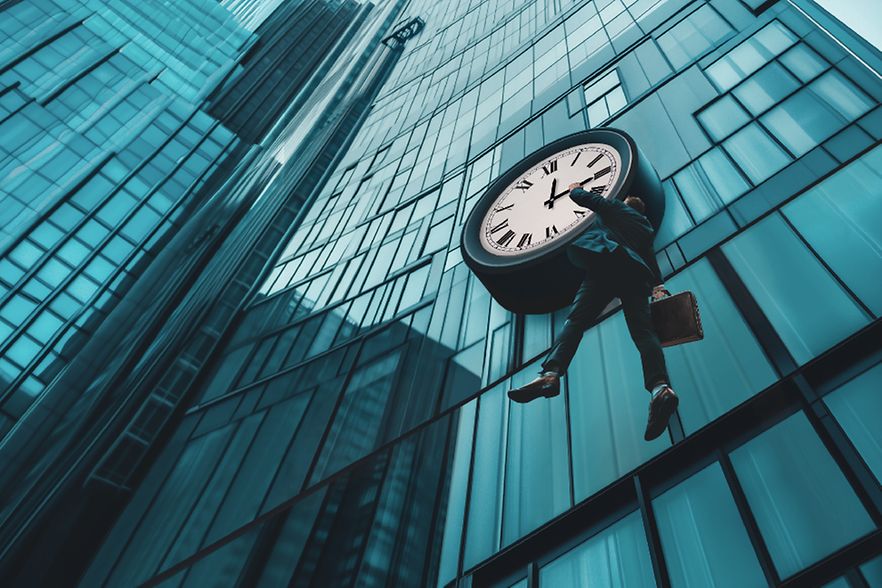 Symbolbild (KI-generiert): Ein Mann h&auml;ngt an den Zeigern einer Uhr, die an der Fassade eines hohen B&uuml;rogeb&auml;udes angebracht ist.