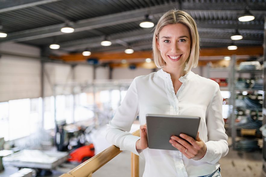 Portr&auml;t einer l&auml;chelnden jungen Frau, die ein Tablet in einer Fabrik benutzt