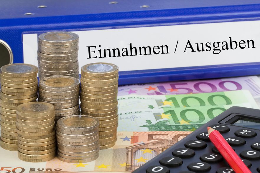 Euro M&uuml;nzen und Scheine. Im Hintergrund liegt ein Ordner mit der Beschriftung Ein- und Ausgaben,