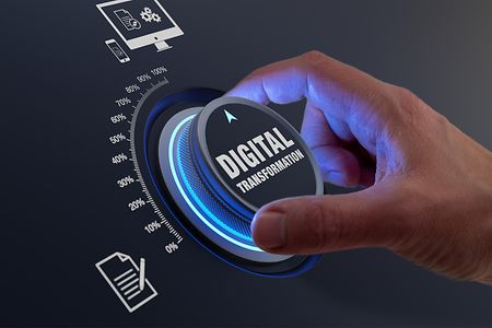 Eine Hand dreht einen Drehknopf mit der Beschriftung "Digital Transformation" auf "100 Prozent".