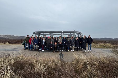 Gruppe aus WJlern steht vor einem Bus mit D&uuml;nen im Hintergrund.