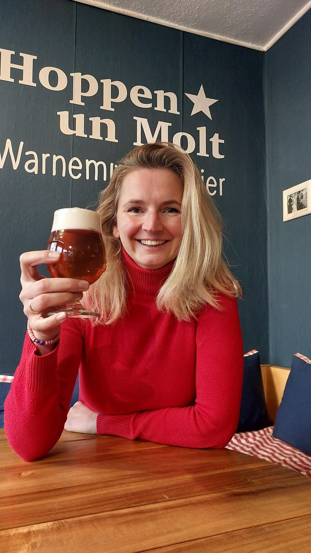 Eine Frau hält ein Bierglas hoch und lächelt in die Kamera