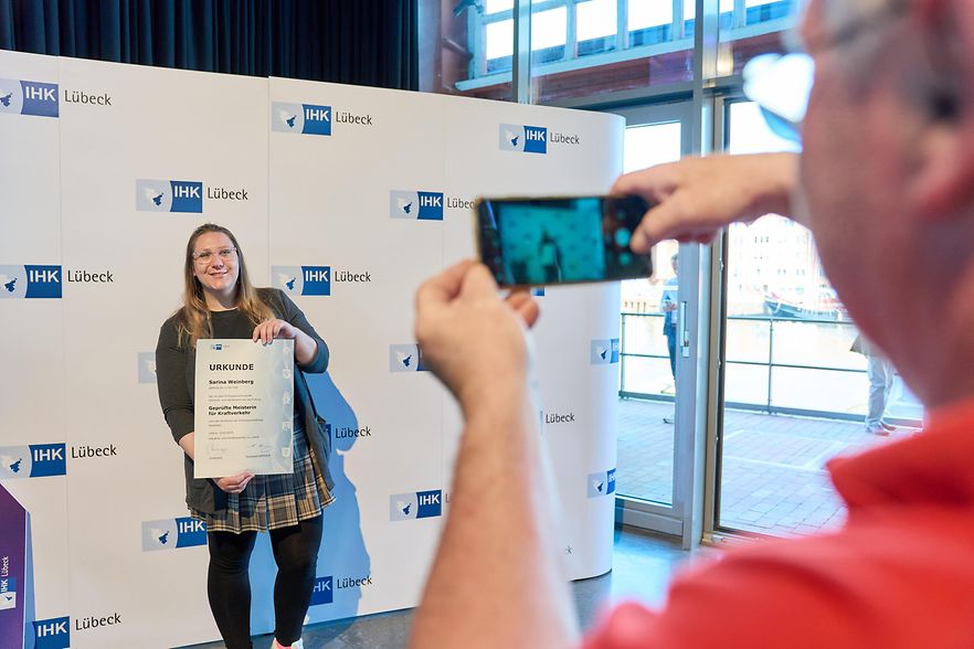 Person h&auml;lt eine Urkunde, w&auml;hrend eine andere Person ein Foto macht.