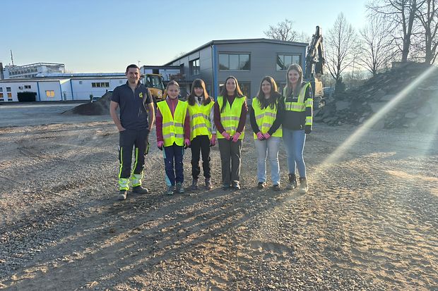 Eine Gruppe von M&auml;dchen und Mitarbeiter der Firma stehen auf einer Baustelle.