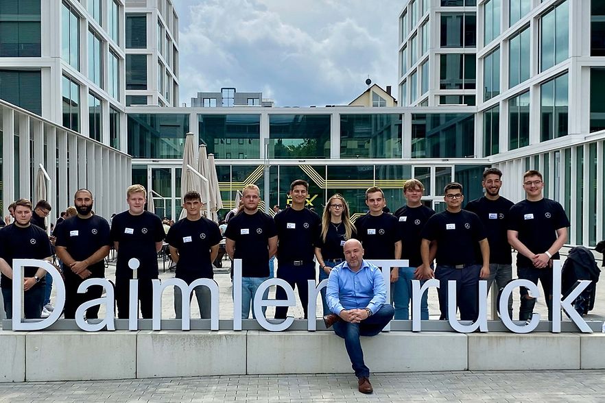 Junge Leute stehen hinter den Buchstaben Daimler Truckm, davor sitzt ein Mann