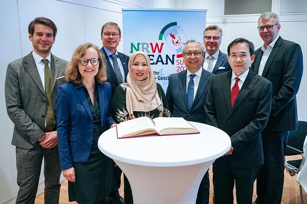 Acht Personen aus Wirtschaft und Politik stehen an einem Stehtisch mit G&auml;stebuch beim NRW-ASEAN Summit 2024.