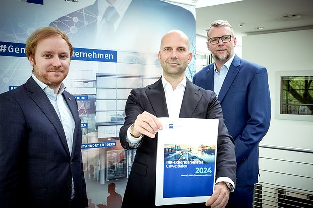 Drei M&auml;nner in Anz&uuml;gen pr&auml;sentieren das IHK-Exportbarometer Ostwestfalen 2024 in einem modernen Raum.