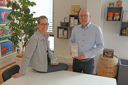 Zwei Personen zeigen Produkte in modernem Raum mit Deko und Regal.