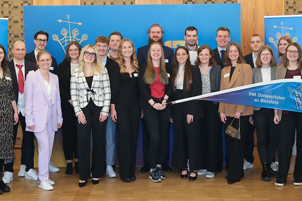Gruppenfoto mit IHK-Ausgezeichneten und Banner mit der Aufschrift &bdquo;IHK Ostwestfalen zu Bielefeld &ndash; Den Besten&ldquo;.