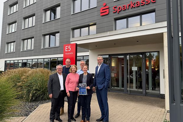 Sechs Personen stehen vor dem Eingang einer Sparkassen-Hauptstelle und halten Konjunkturbericht in die Kamera.