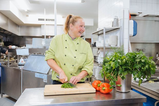 Eine Frau schneidet Petersilie in einer Restaurantk&uuml;che.
