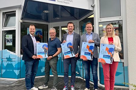 5 Personen stehen vor einem Eingang mit Logo IHK Koblenz und halten Plakate in den H&auml;nden