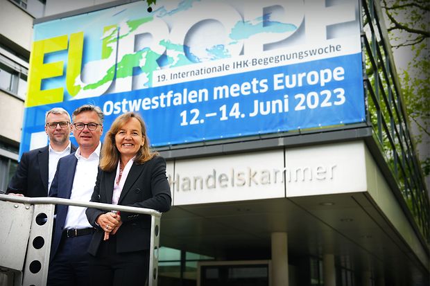 Drei Personen stehen vor der IHK mit einem Banner zur Veranstaltung &bdquo;Ostwestfalen meets Europe&ldquo; im Juni 2023.