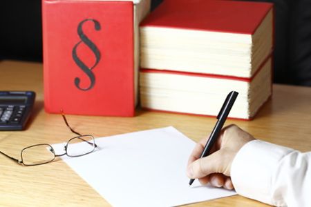 Mann schreibt am Schreibtisch, auf dem Taschenrechner, Brille und Gesetzb&uuml;cher liegen