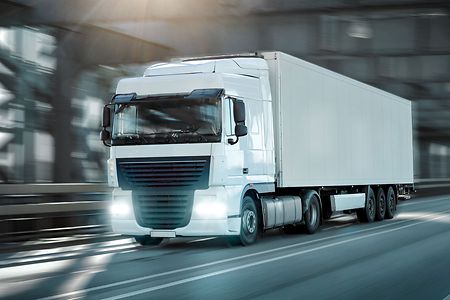 Wei&szlig;er Lkw f&auml;hrt auf einer Stra&szlig;e mit eingeschaltetem Licht.
