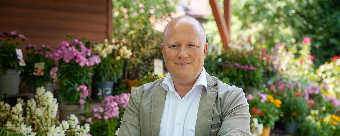 Peter Zens betreibt den Gertrudenhof in K&ouml;ln. Hier steht er vor bunten Blumen. 