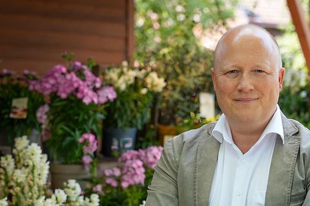 Peter Zens betreibt den Gertrudenhof in K&ouml;ln. Hier steht er vor bunten Blumen. 