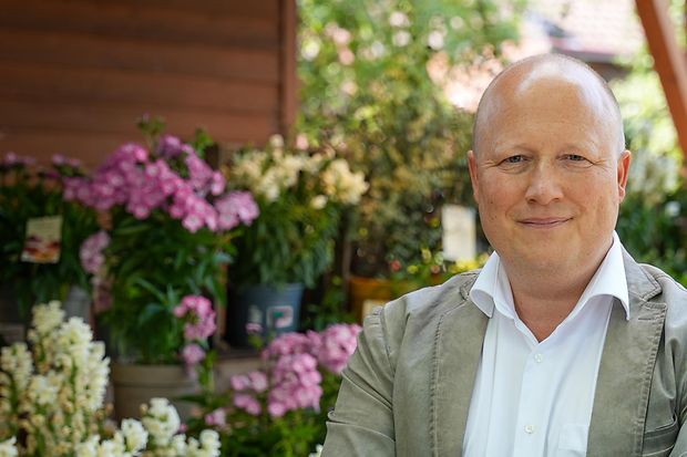 Peter Zens betreibt den Gertrudenhof in K&ouml;ln. Hier steht er vor bunten Blumen. 