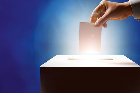 Eine Hand wirft einen leeren Wahlzettel in eine Wahlurne (KI-generiert)