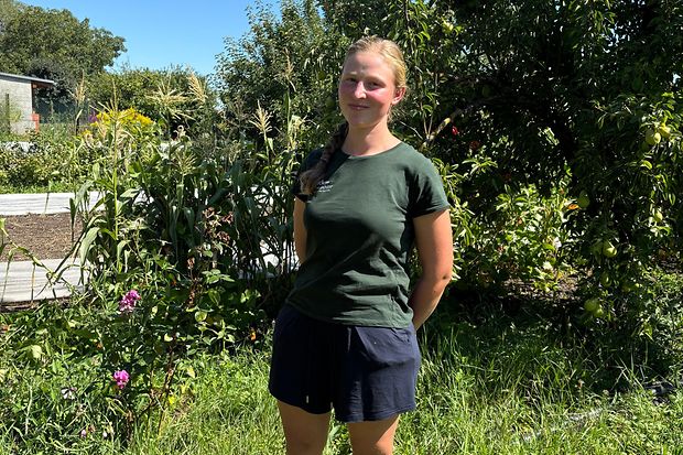Sarah Holz vom H&ouml;lzer Hof l&auml;chelt in die Kamera umringt von Pflanzen und B&auml;umen