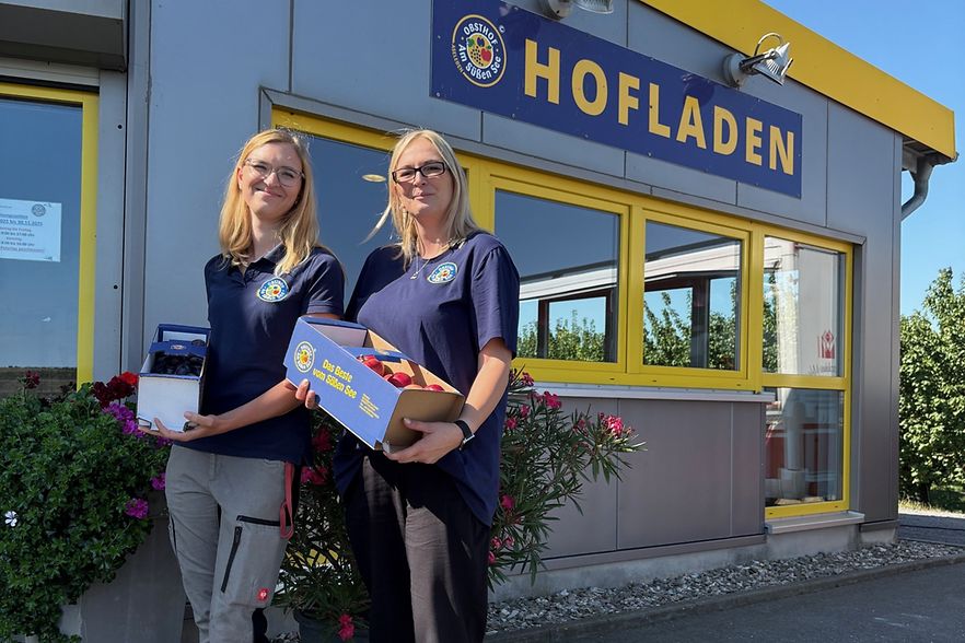 Yvette Krause und Susanne Hesse stehen vor dem Hofladen vom Obsthof Am S&uuml;&szlig;en See mit Papptr&auml;gern gef&uuml;llt mit &Auml;pfeln und Pflaumen