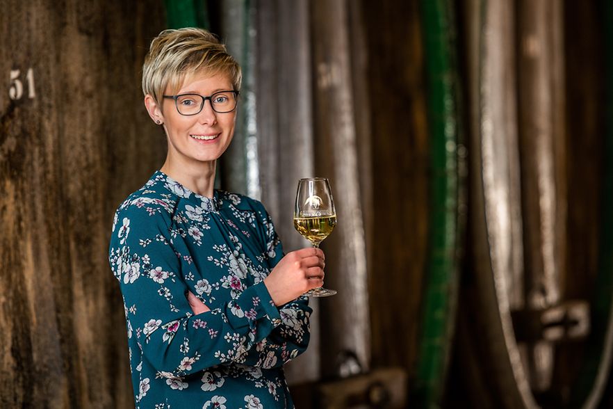 Kellermeisterin Kathleen Romberg l&auml;chelt in die Kamera mit einem Glas Wei&szlig;wein in der rechten Hand