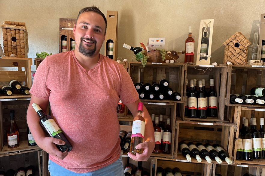 Herr Gaudig pr&auml;sentiert zwei Weinflaschen vor einem Weinregal