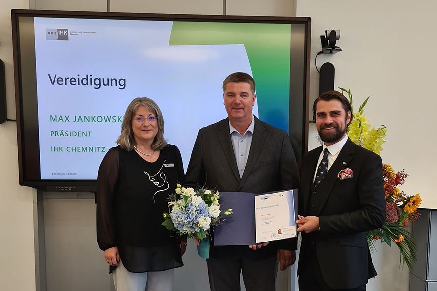 Eine Frau und zwei M&auml;nner stehend mit Urkunde und Blumenstrau&szlig; in der Hand