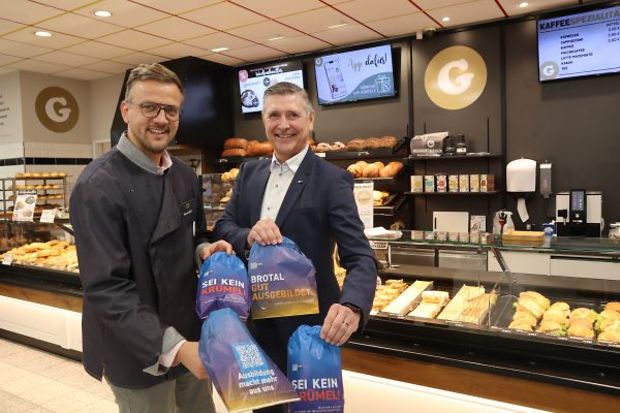 Zwei Männer in einer Bäckerei halten Brottüten mit Ausbildungswerbung in der Hand.