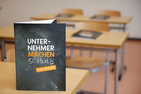 Werbekarte "Unternehmer machen Schule" steht auf Schulbank