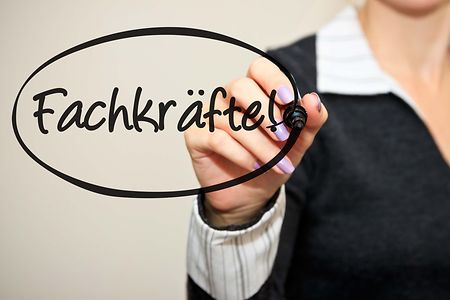 Person schreibt &bdquo;Fachkr&auml;fte&ldquo; mit Marker auf Glasfl&auml;che.