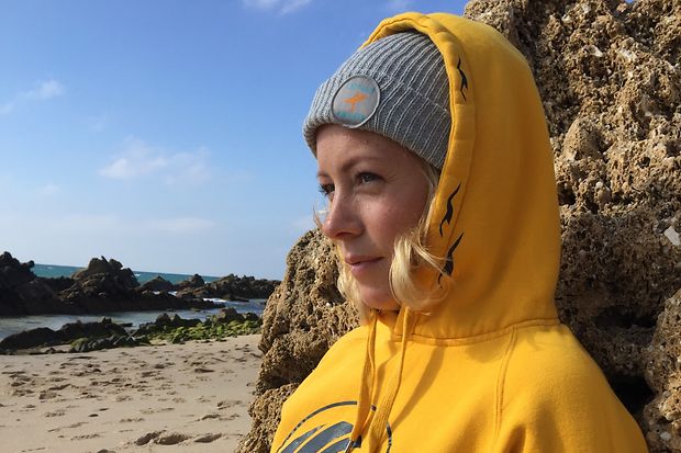 Nora Kim de Vries von Tofree North sitzt am Felsen gelehnt am Strand mit Blick aufs Meer.