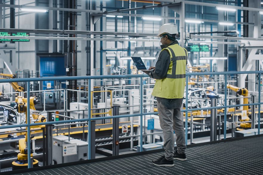 Ein Mann mit einem Laptop steht in einer Industriehalle. 