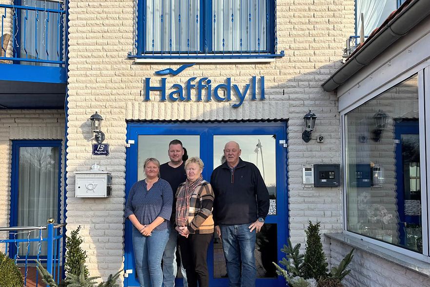 Eine Familie steht vor einem Haus mit der Aufschrift "Haffidyll".