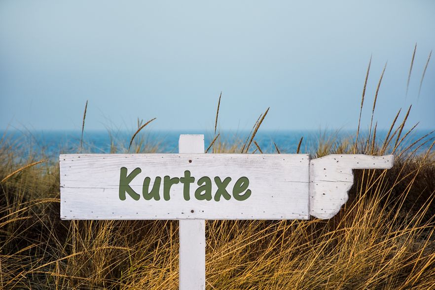 Hinter einer D&uuml;ne steht ein Schild mit der Aufschrift "Kurtaxe".