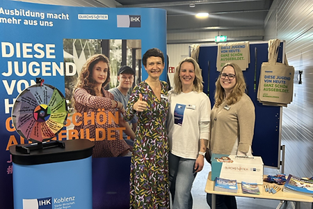 Drei Frauen stehen vor einem Messestand zum Thema Ausbildung.