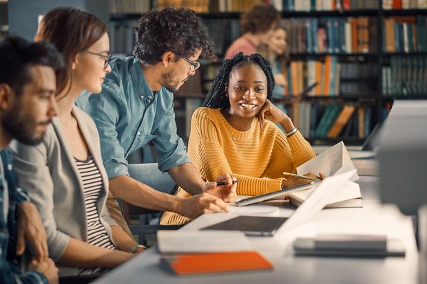 Studenten sitzen zusammen und diskutieren vor einem Laptop und Dokumenten.