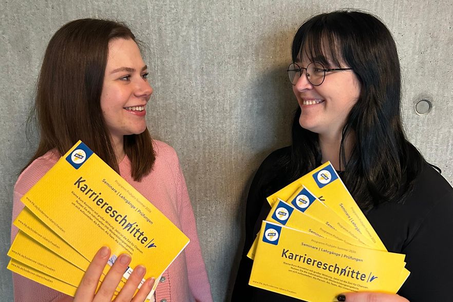 Zwei Frauen halten die neuen Weiterbildungsprogramme in den H&auml;nden und l&auml;cheln sich an.