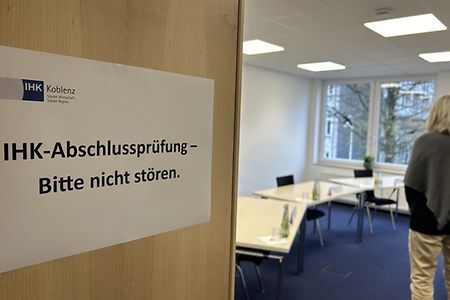 Ein Schild h&auml;ngt an einer T&uuml;r: "IHK-Abschlusspr&uuml;fungen - Bitte nicht st&ouml;ren". Pr&uuml;fungsraum mit Person im Hintergrund.