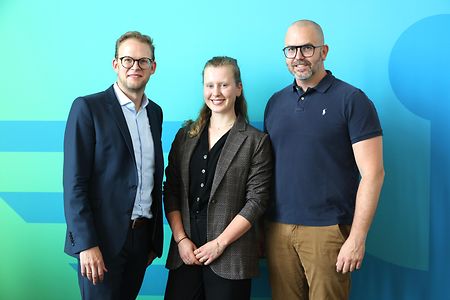 Teilnehmer des Forums stehen vor einer blauen Wand und l&auml;cheln in die Kamera.