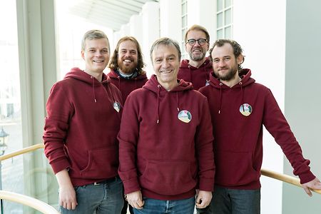 Man sieht eine eine Gruppe von f&uuml;nf M&auml;nnern in roten Kapuzenpullovern.