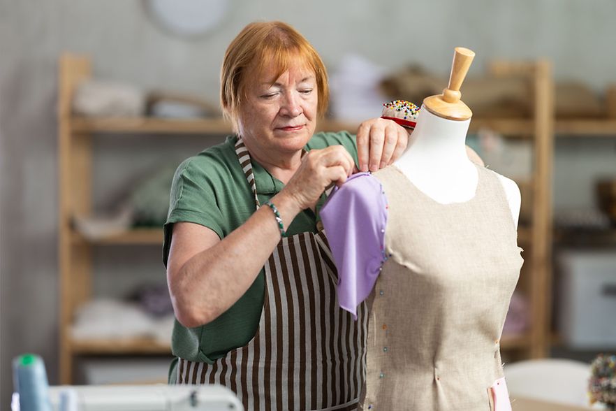 Mature,Female,Tailor,Sews,New,Dress,On,A,Mannequin,In