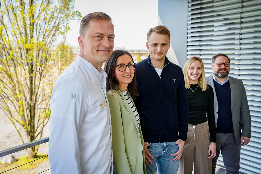 F&uuml;nf Personen stehen auf einem Balkon vor einem B&uuml;rogeb&auml;ude