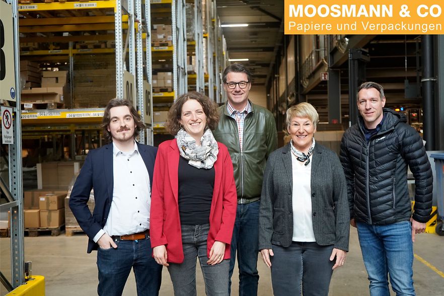 F&uuml;nf Personen stehen im Lager der Firma MOOSMANN & CO und l&auml;cheln in die Kamera.