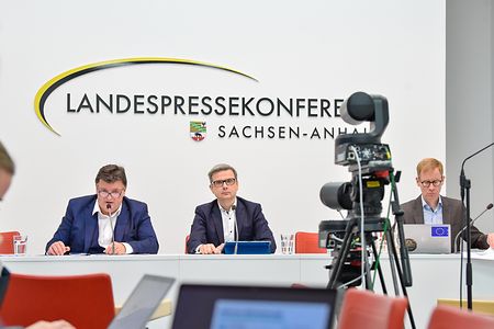 Pressekonferenz Sachsen-Anhalt mit drei Personen am Tisch und Kamera im Vordergrund