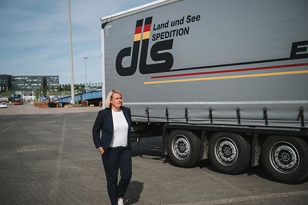 Eine Frau im dunklen Hosenanzug geht an einem Lkw vorbei, der auf einem Parkplatz parkt.