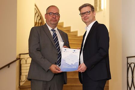 Zwei Personen pr&auml;sentieren in einem Treppenhaus einen Wirtschaftsbericht.