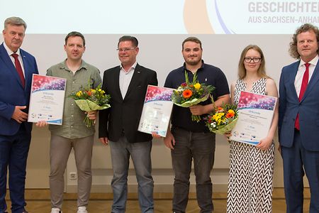 Gruppenfoto bei einer Preisverleihung mit Urkunden und Blumen.