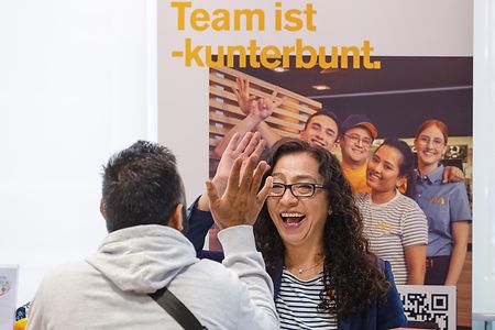 Eine Frau und ein Mann sitzen sich an einem Tisch gegen&uuml;ber. Beide lachen und geben sich High Five.