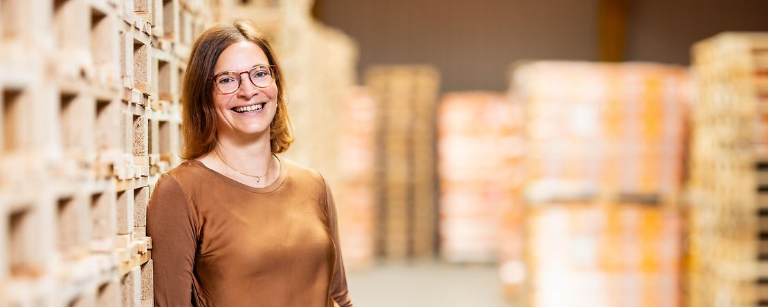 Frau steht l&auml;chelnd vor B&uuml;cherregalen